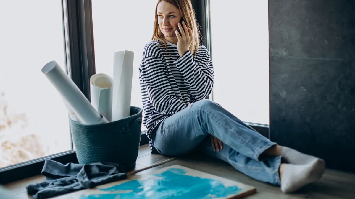 A woman on the phone in a bright studio with rolled plans beside her