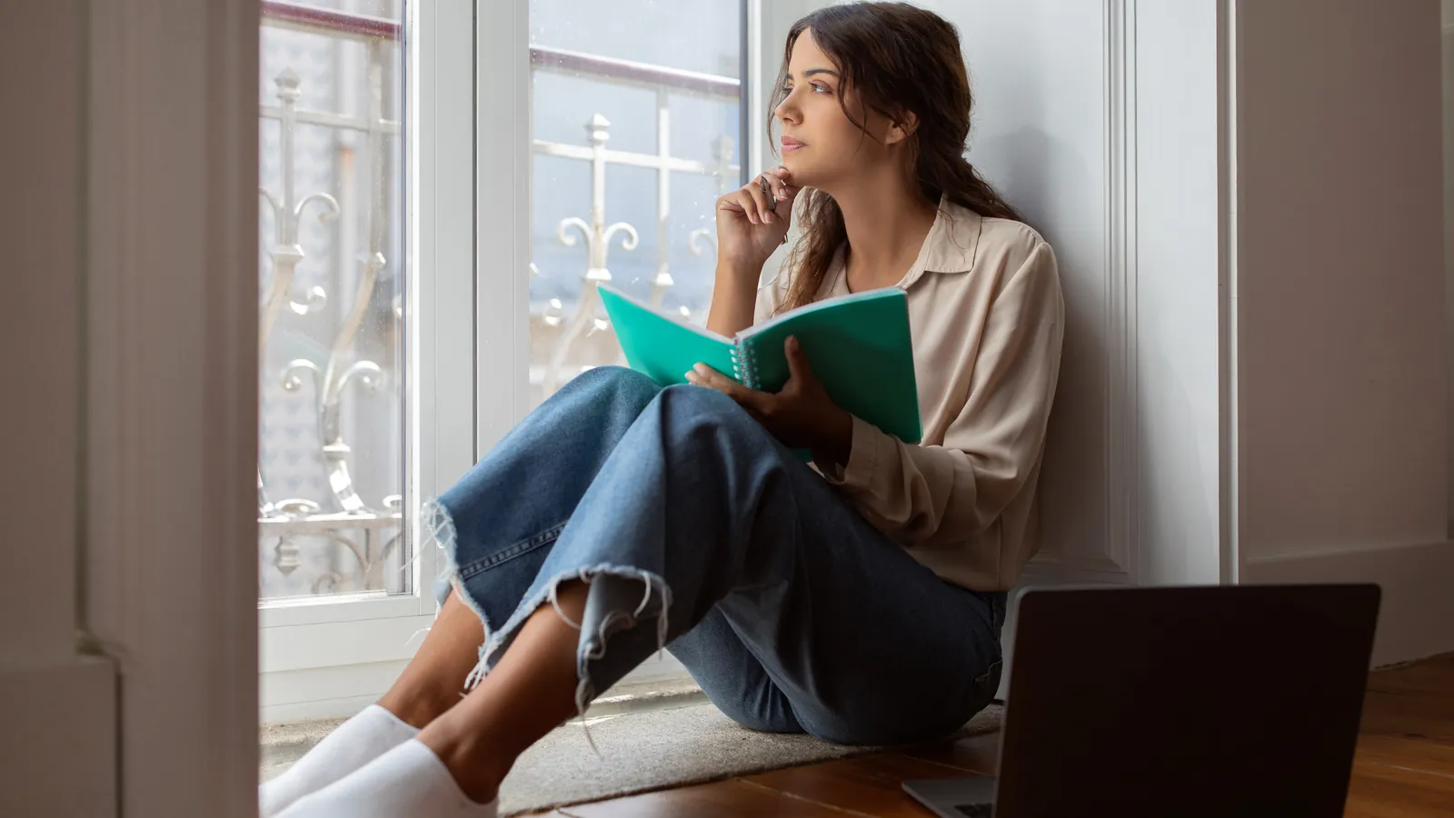 quarter life crisis: a young woman with a notebook looking out of a window