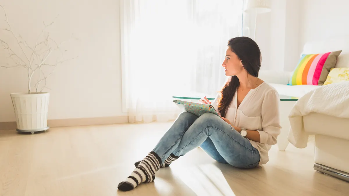 A young woman sitting on the floor of a bright room, thinking quietly