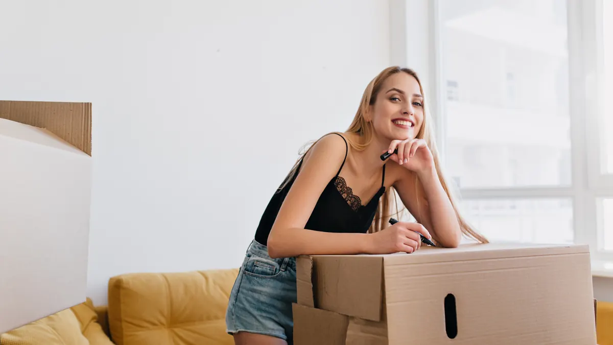 A woman labeling a cardboard box as she packs to move