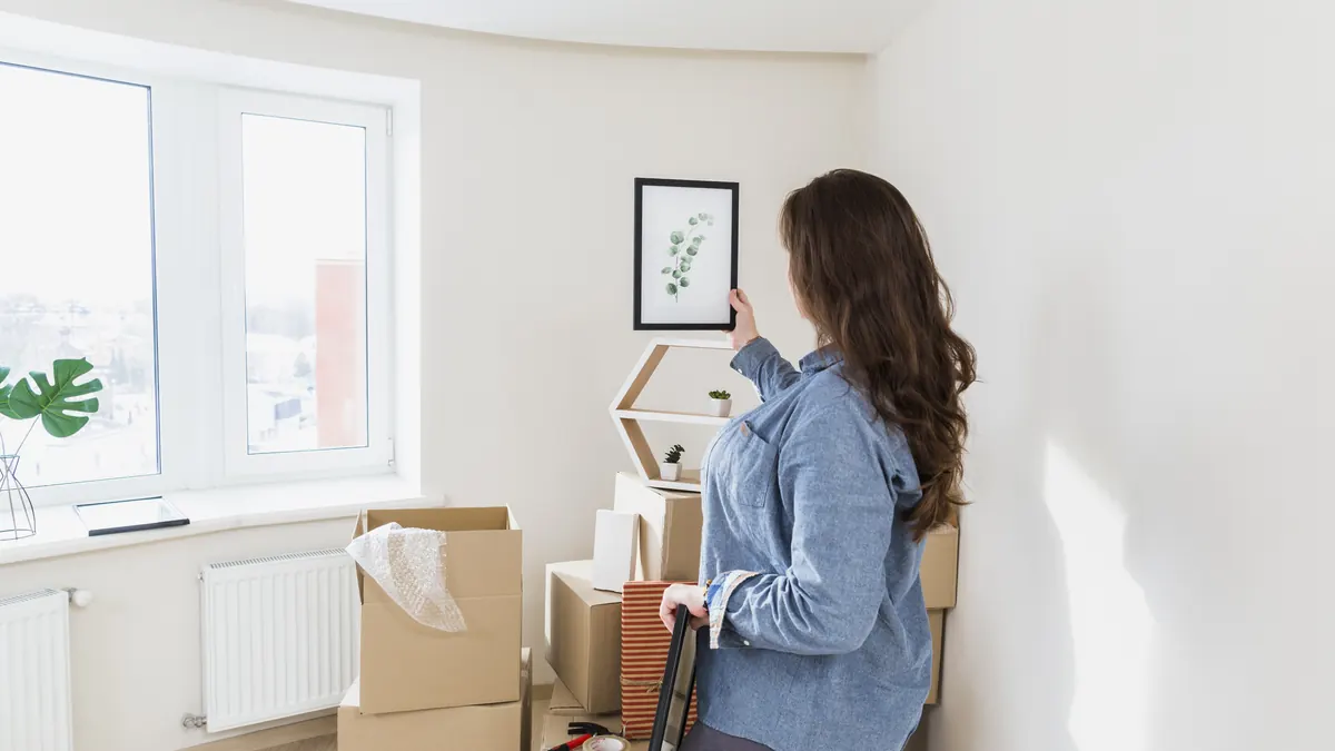 A woman hanging a framed leaf print on the wall of her new home